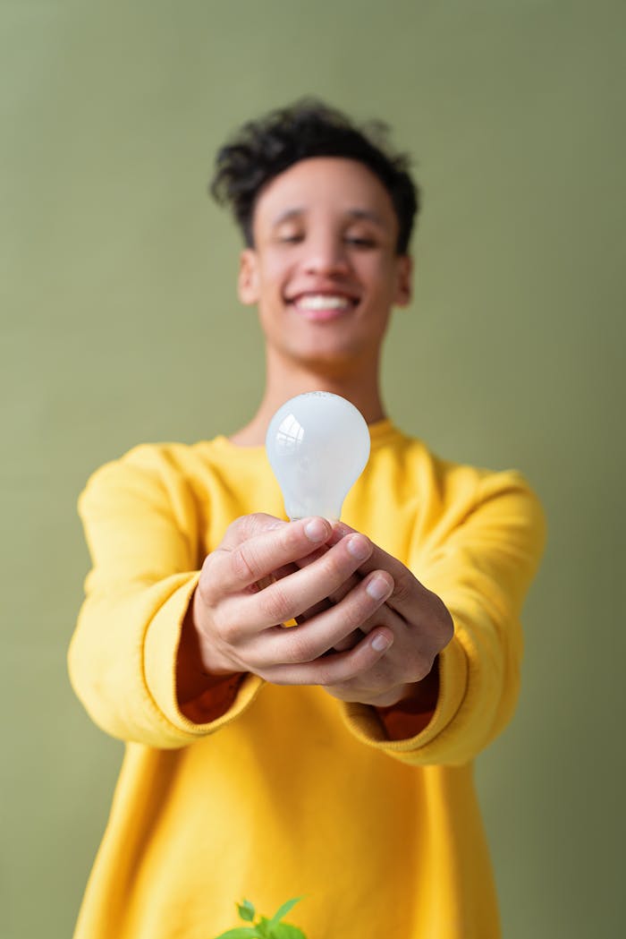 Cheerful adult holding a lightbulb with a green background, symbolizing innovation or ideas.